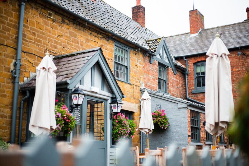 The front of The Chequers, a red-brick country pub with hanging flower baskets and white parasols